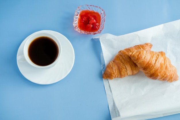 Croissants con mermelada y café de la mañana yacía aislado sobre fondo azul.