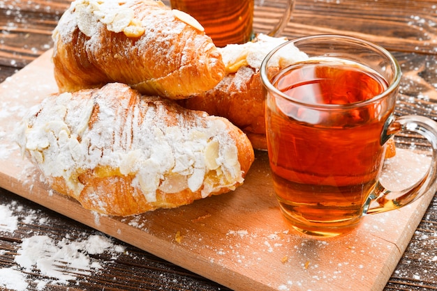 Croissants mit Mandeln und Tee auf einem Holztisch.