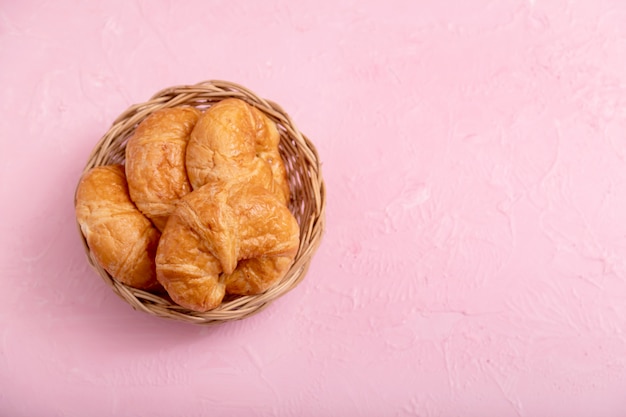 Croissants na cesta de madeira no fundo rosa