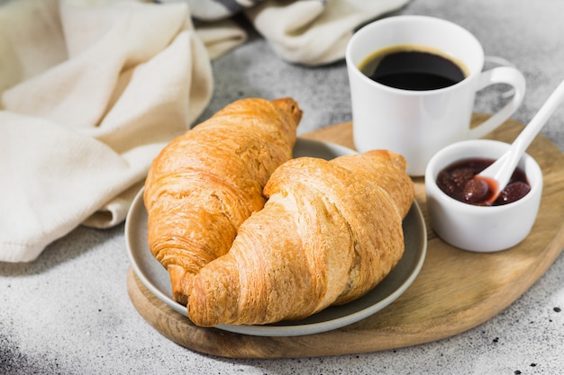 Croissants en un plato con café y mermelada de fresa. Pasteles para el desayuno