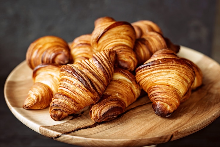 Foto croissants recém-assados. croissants de manteiga e pãezinhos quentes e perfumados em um suporte de madeira