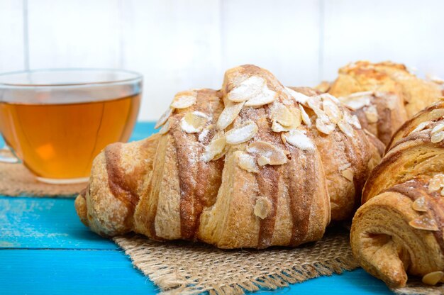 Croissants recién horneados con copos de almendras, taza de té sobre un fondo de madera azul. Repostería francesa. Desayuno.