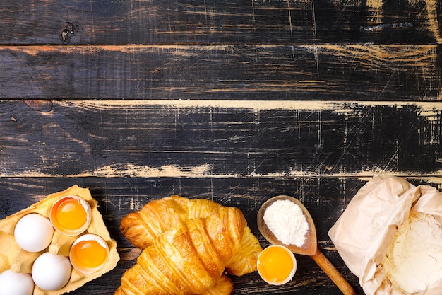 Croissants recién horneados con harina, cuchara de madera, huevos y yemas de huevo