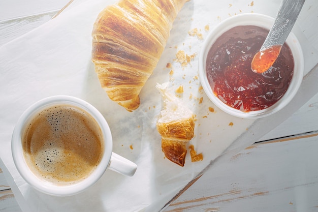 Croissants recién horneados con mermelada y café en la mesa al sol de la mañana delicioso concepto de desayuno