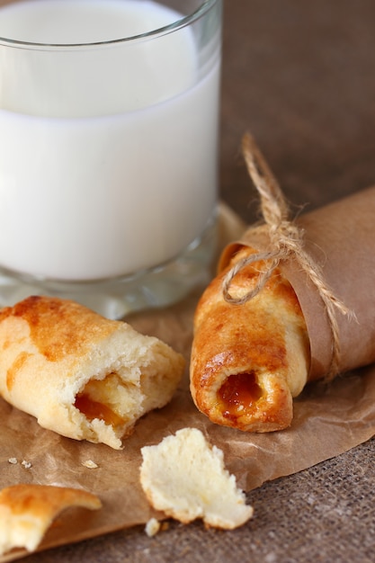 Croissants rotos y migas con mermelada de durazno envueltos en papel de regalo kraft y atados con hilos con lazos y un vaso de leche sobre un mantel gris áspero