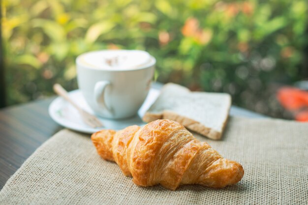 Croissants sabrosos recién horneados con taza de café en madera