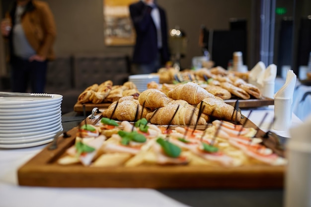 Croissants, Sandwiches und Muffins liegen beim Frühstück in einem Hotel auf Holztabletts auf einem Tisch mit weißer Tischdecke