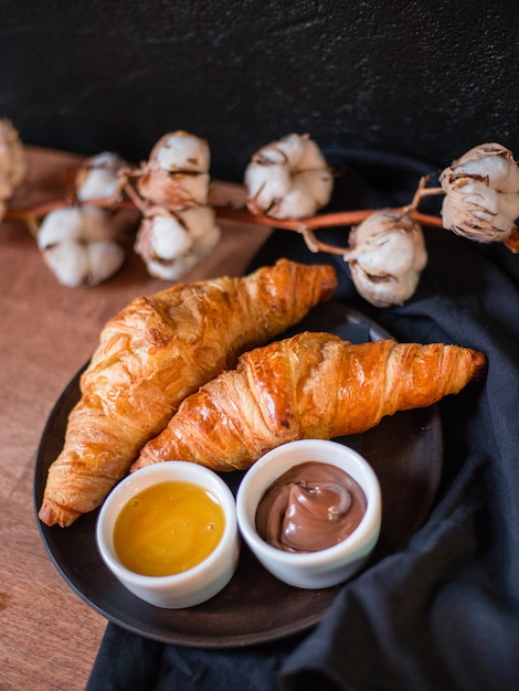 Croissants, schokolade und honig. woden platte mit köstlichem frühstück, baumwollblume