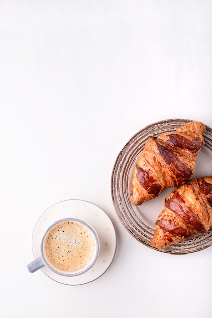 Croissants y una taza de café en una mesa de madera blanca