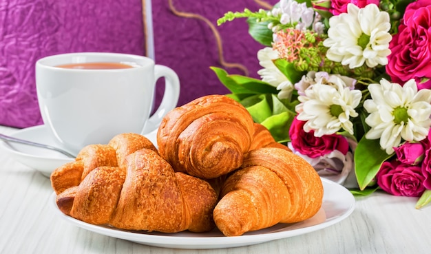 Croissants, taza de té y ramo de flores.