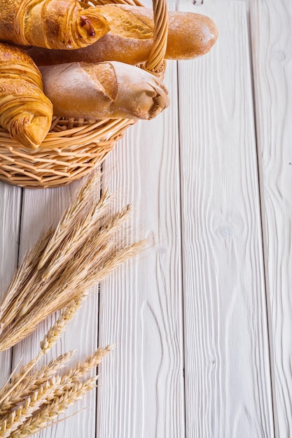 Croissants und Baguettes in Weidenkorb-Ähren auf weißen Holzbrettern mit Copyspace