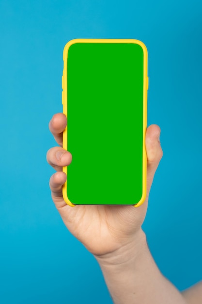 Croma verde en la pantalla del teléfono Mano que sostiene el teléfono inteligente colorido sobre fondo azul