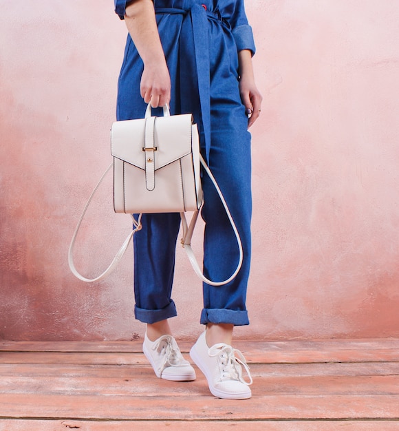 Crop Foto einer Frau, die einen modischen Lederrucksack in ihrer Hand gegen den Tisch einer Lehmwand hält. Modekonzept