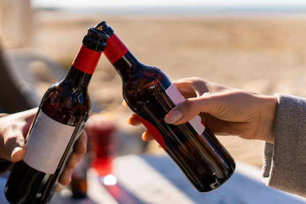 Crop Hände klirren Bierflaschen am Strand