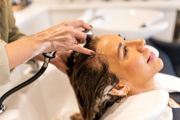Crop Hairstylist wäscht die Haare einer Kundin in einem Waschbecken mit Wasserhahn