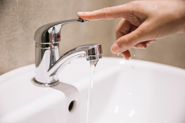 Crop Hand berühren Wasserhahn mit strömendem Wasser