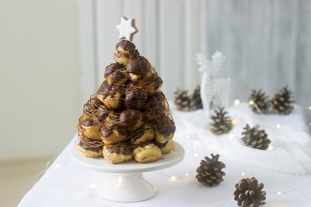 Croquembouche-Torte in Weihnachts- oder Neujahrsdekoration mit Tannenzapfengirlande und Hirschfigur.