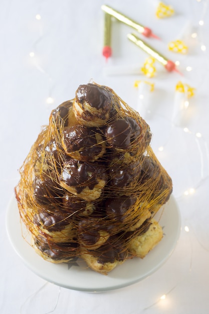 Croquembush feito de profiteroles com creme e chocolate, decorado com fios de caramelo.