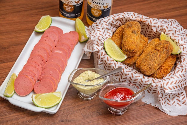 Croqueta de pollo y salchicha Cambui, bocadillo típico brasileño servido con rodajas de limón, salsa de chili y mayonesa En una mesa de madera servida con la famosa cerveza corona