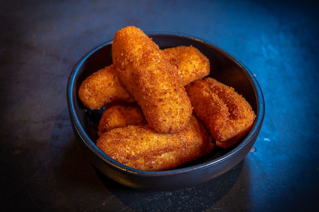 Croquetes de presunto em fundo preto e com luz azul, em prato ou tigela preta