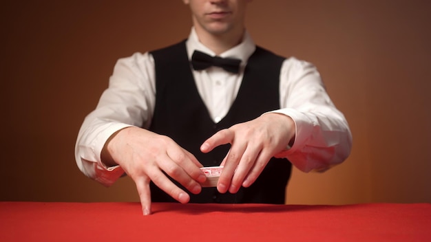 El croupier masculino joven baraja las cartas antes del comienzo de la mesa roja del juego