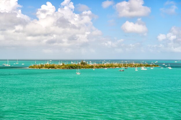 Crucero en barcos turísticos o yates flotando cerca de la isla con casas y árboles verdes en agua turquesa y cielo nublado azul, navegación y deporte, viajes y vacaciones, Key West Florida, EE. UU.