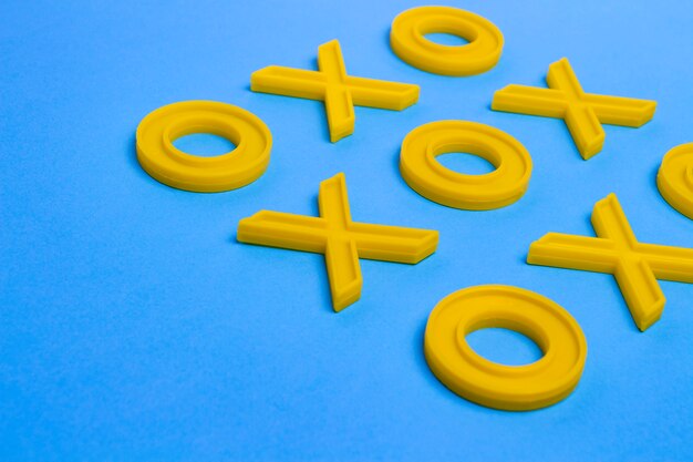 Cruces de plástico amarillo y ceros para jugar al tic-tac-toe en una superficie azul. Concepto XO Win Challenge. Juego educativo para niños