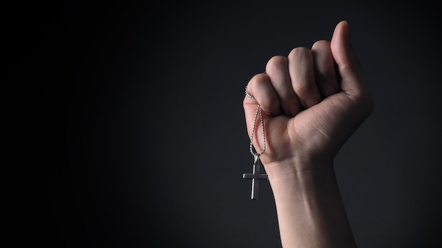 Crucifijo de plata o colgante y collar de cruz en el cuerpo o en la mano Foto de estudio de fondo de color negro