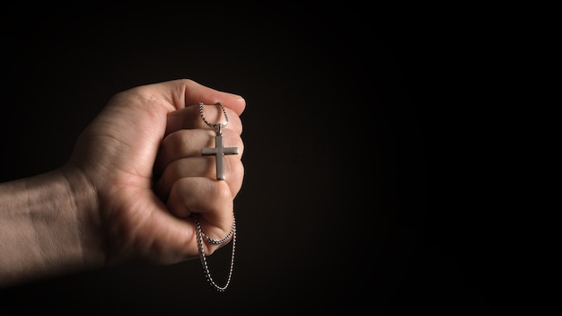 Crucifixo de prata ou pingente em cruz e colar no corpo ou na mão com fundo de cor preta