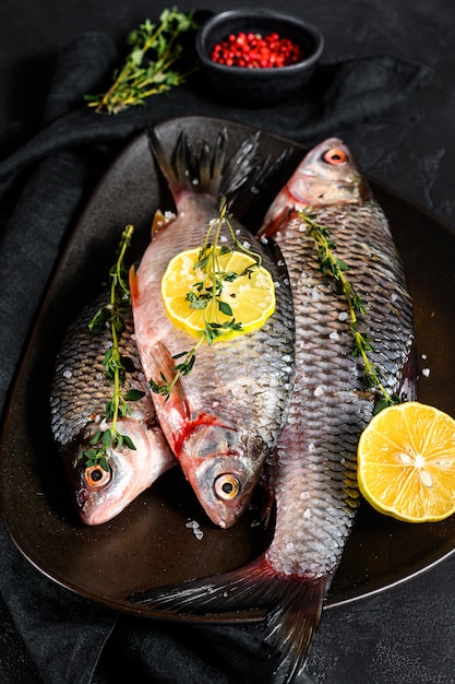 Crudo carpa crucian con limón y tomillo en un plato negro. Pescado orgánico de río. Vista superior