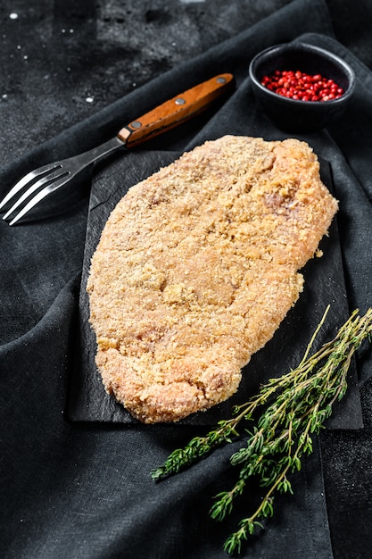 Foto crudo wiener schnitzel, filete empanado listo para cocinar. superficie negra. vista superior