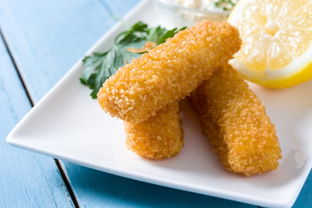 Crujientes palitos de pescado frito con limón y salsa en madera azul