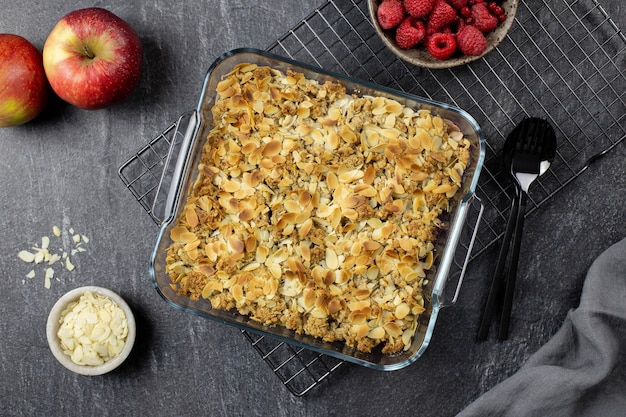 Crumble de arándano y manzana, crujiente en una fuente para hornear de vidrio con hojuelas de almendras y bayas frescas sobre fondo de hormigón de piedra oscura. Vista superior.