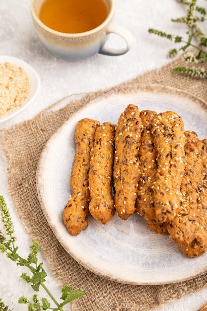 Crumble cookies com seasme e amêndoas na placa de cerâmica com uma xícara de chá verde na vista lateral de fundo de concreto cinza fechar o foco seletivo