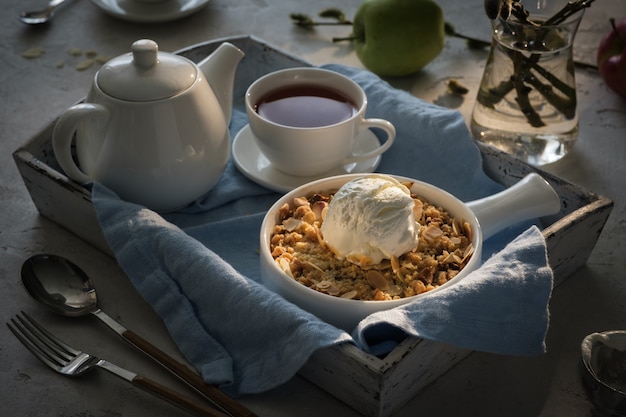 Crumble de maçã com uma bola de sorvete de baunilha e chá em uma bandeja de madeira. conceito de café da manhã