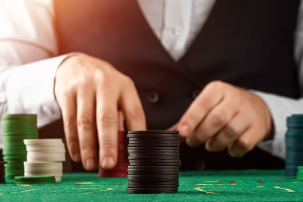 Crupiê de mãos masculinas em um cassino e jogando fichas em um pano verde closeup