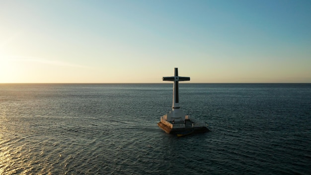 cruz católica em cemitério afundado no mar ao pôr-do-sol drone aéreo grande crucifixo marcando o