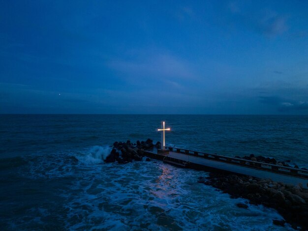 Cruz cristã em pé no cais no mar ou oceano com céu dramático à noite