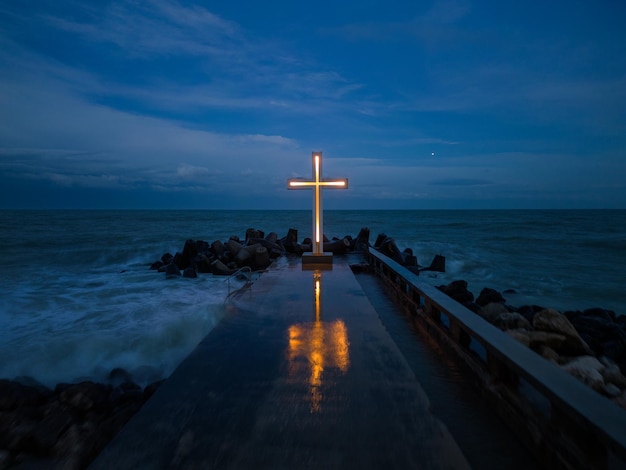 Cruz cristã em pé no cais no mar ou oceano com céu dramático à noite