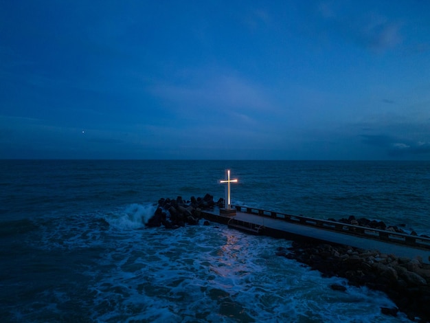 Cruz cristiana de pie en el muelle en el mar o el océano con un cielo dramático por la noche