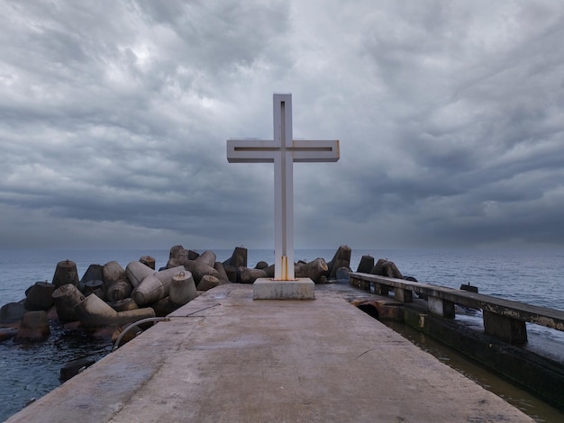 Cruz cristiana de pie en el muelle en el mar o el océano con un cielo dramático