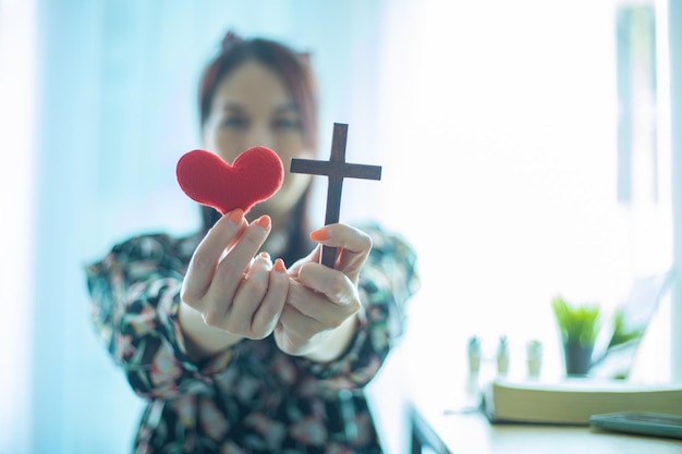 Cruz de madeira e coração vermelho na mão feminina com conceito de amor e religião