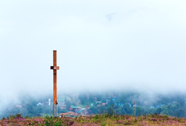 Cruz de madeira no topo da colina de flores de urze de verão e vista do campo de manhã nublada atrás