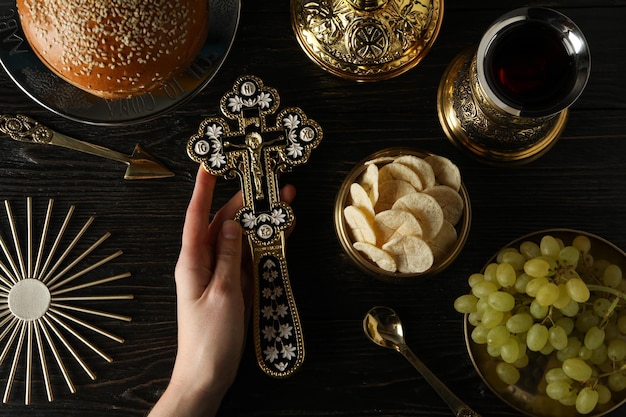 Cruz de pão na mão uvas em tigela dourada e copo de vinho em fundo de madeira vista superior