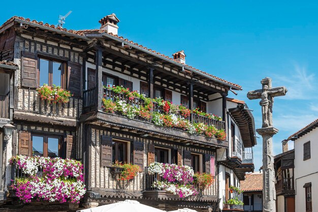 Cruz de piedra del siglo XVIII y hermosa arquitectura tradicional con balcones adornados con macetas y tiestos in der mittelalterlichen Villa von La Alberca Espana