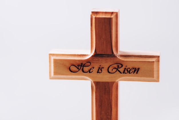 Cruz de madera con texto Él es resucitado sobre fondo gris Recordatorio del sacrificio de Jesús y la resurrección de Cristo Pascua Eucaristía concepto cristianismo símbolo y fe