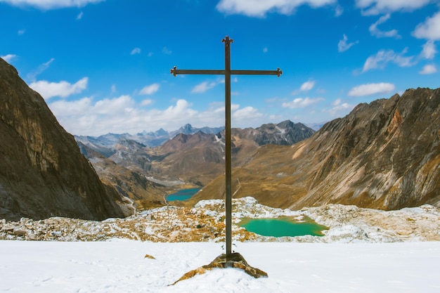 Una cruz de metal encima de un pico nevado y un paisaje de montañas