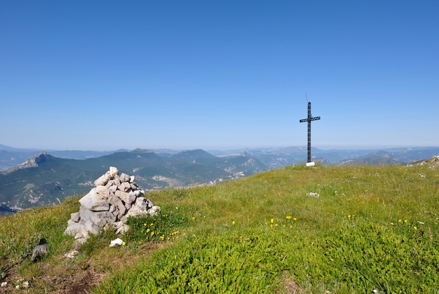 Cruz de pie en una cresta verde junto a un montón de piedras bajo un cielo azul