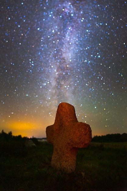 Cruz de piedra en el antiguo cementerio bajo el cielo estrellado.