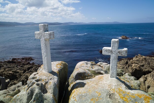 Foto cruz en las rocas por el mar contra el cielo